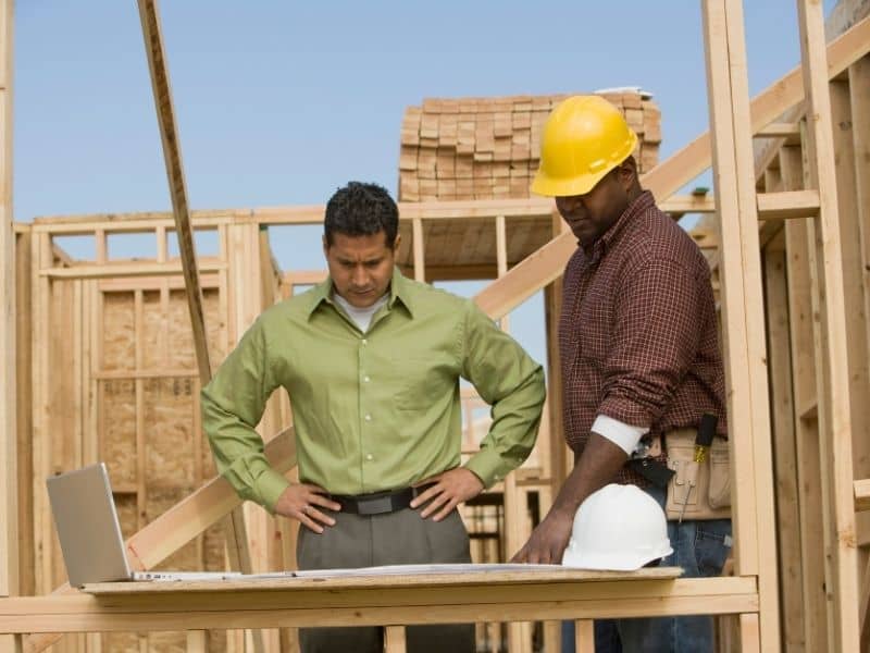 Construction professionals reviewing blueprints and site plans on a building site to ensure accurate construction survey planning before work begins.