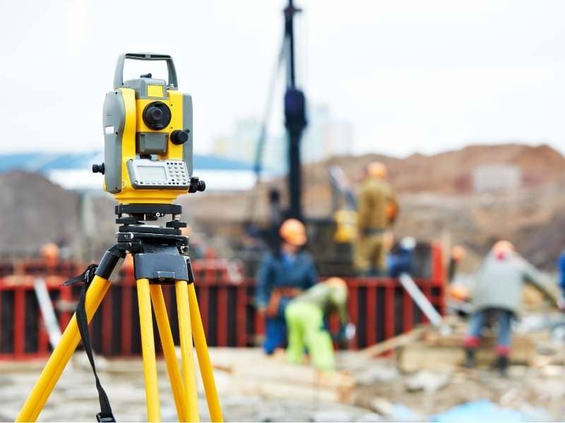 Construction Surveyors Carrollton Georgia | Carrollton Land Surveying Yellow surveying instrument on a tripod at a construction site with workers in the background.